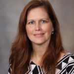 Dr. Kelly Flemming professional headshot. Head and shoulders of smiling woman with long red hair.