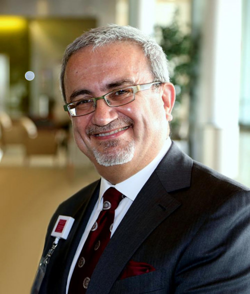 Dr. Issam Awad, a white man with grey hair. He is smiling, wearing glasses, a white dress shirt, tie, and a jacket.