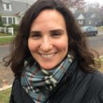Photo of Dinah Winchester, a white woman with wavy brown hair smiling.