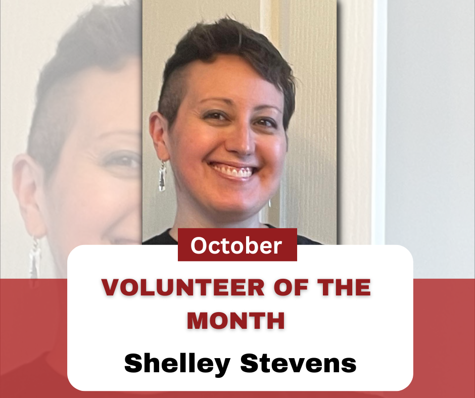 October Volunteer of the Month Shelley Stevens. Photo of a woman smiling, she has short dark hair, and dangly earrings.