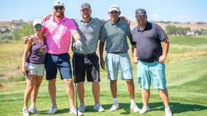 A group of 5 individuals standing on the golf course smiling.