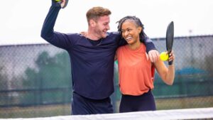A man and a women with their arms over the others shoulder holding pickleball paddles and smiling.