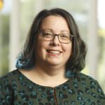 Headshot of Angela Glading, a smiling white woman with shoulder-length brown hair, wearing glasses.